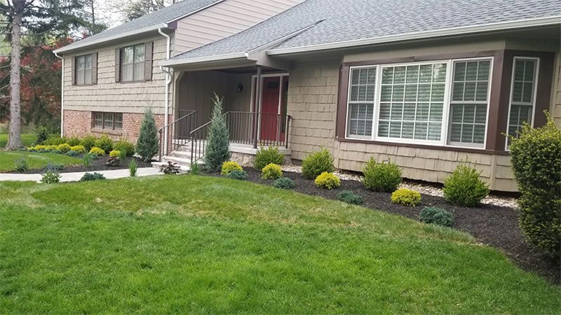 A house with a green lawn and a landscaped garden bed. The front door is red.