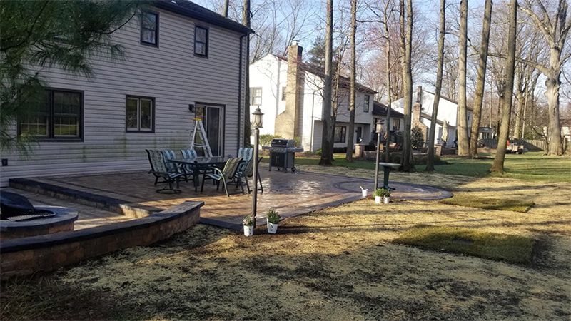 Backyard with patio, furniture, fire pit, and newly planted grass, trees in background.