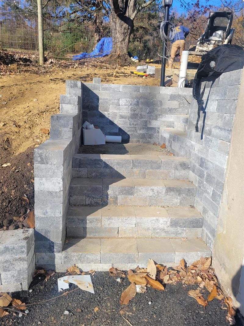 Stone steps leading up from a dark ground, partially constructed. A person works in the background.