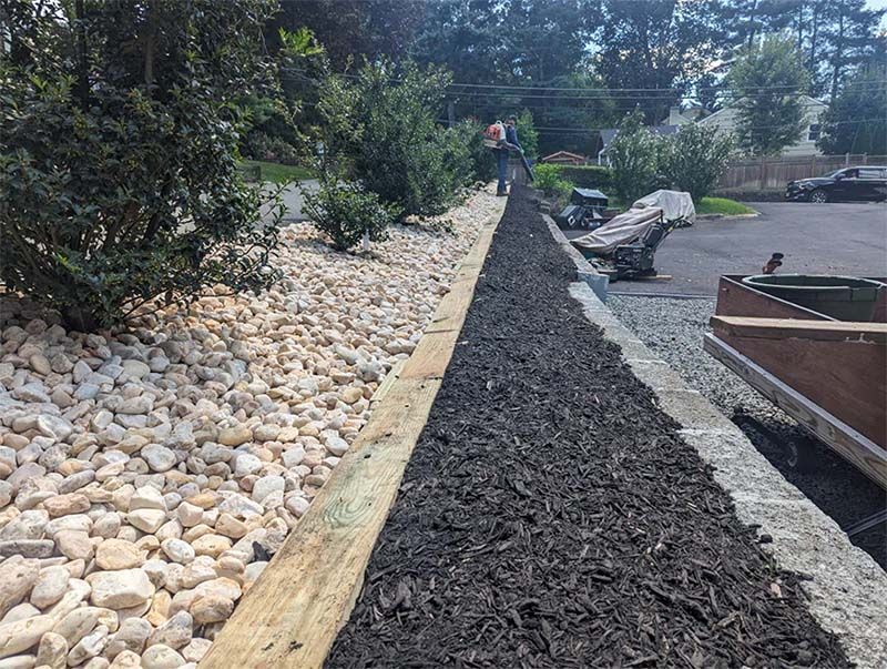 A wooden fence is surrounded by rocks and mulch.