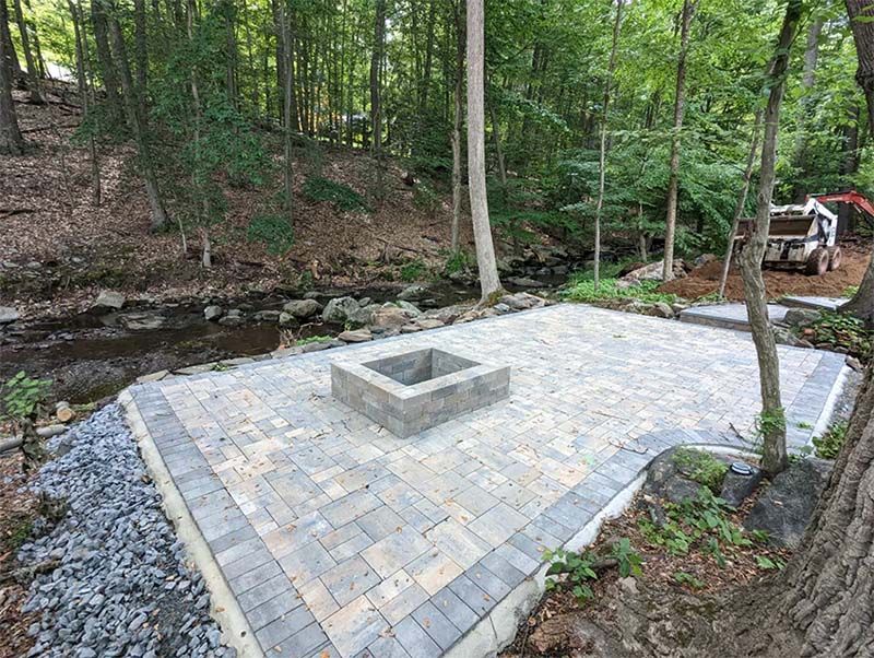 A fire pit in the middle of a patio in the woods.