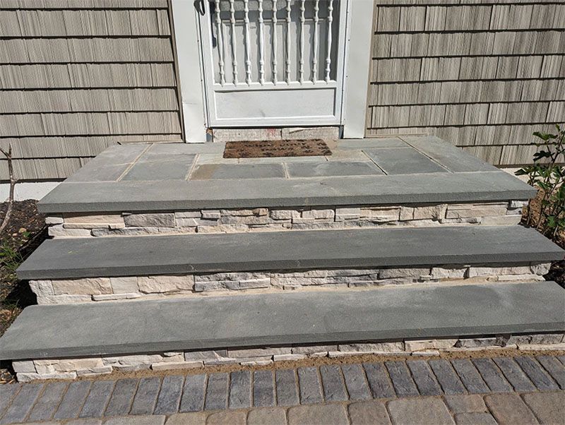 Stone steps leading to a doorway with light gray siding and a security screen.
