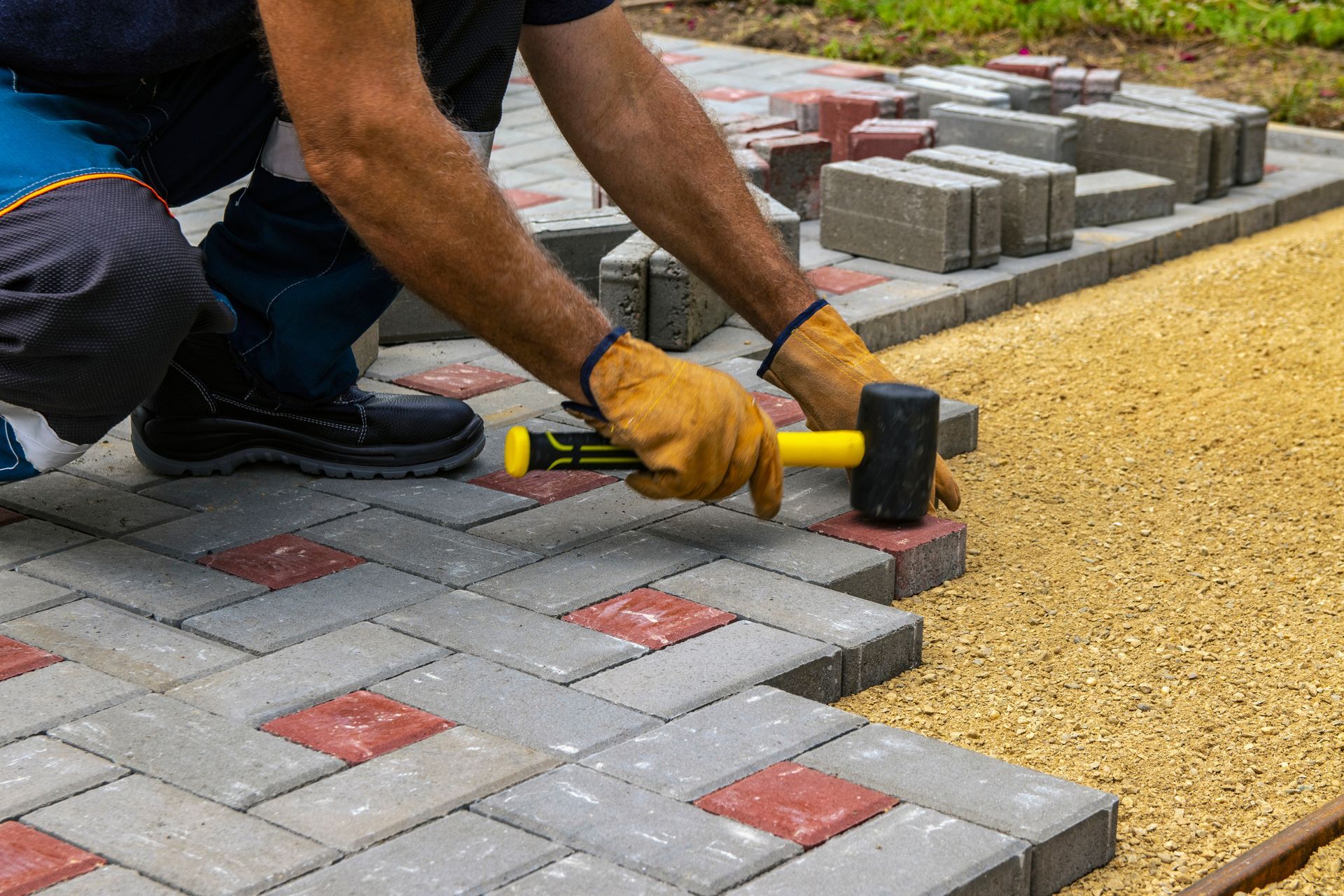 A man is laying bricks on a sidewalk with a hammer.