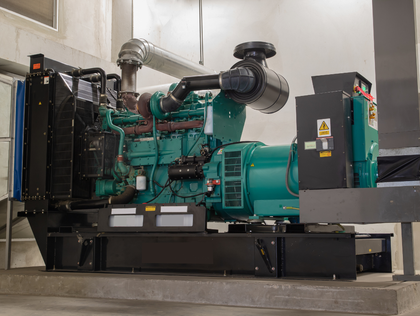 A large, teal generator in a concrete room with a black frame and metal exhaust pipes.