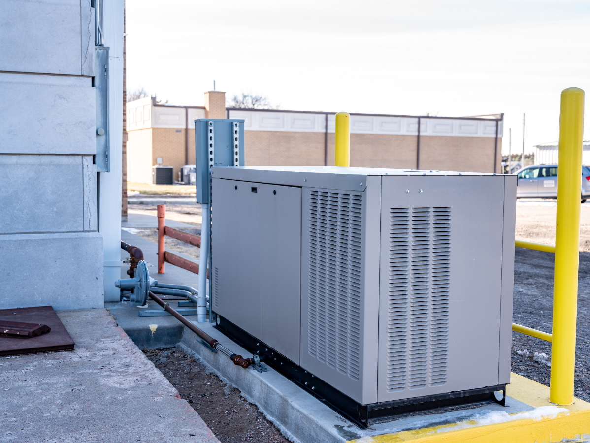 Gray generator outside a building with yellow posts for protection.