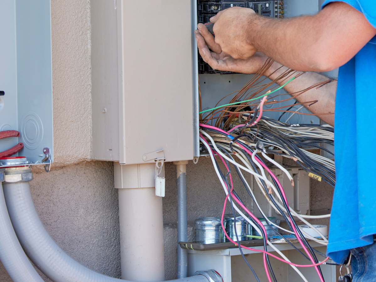 Electrician working inside an open electrical panel with colored wires.