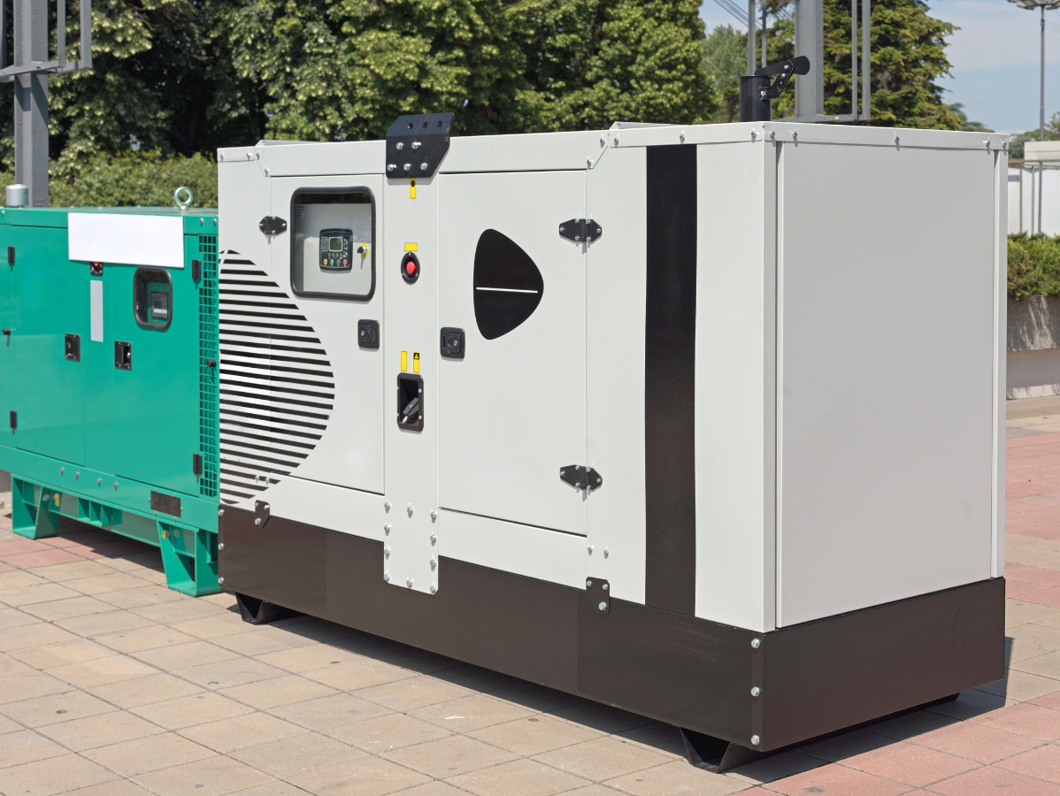Two large industrial generators, one green and one gray, outdoors.