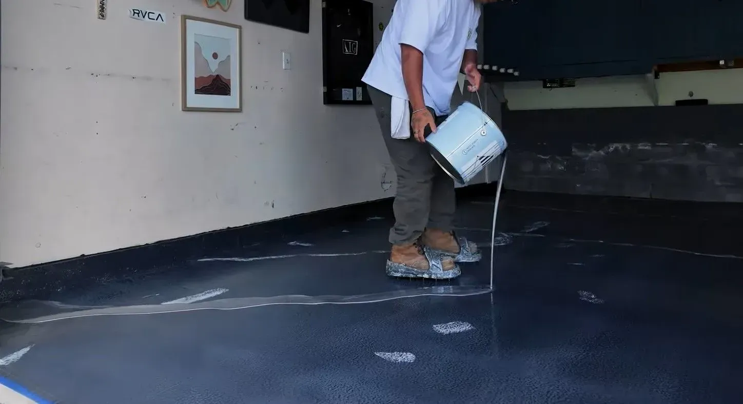 Worker pouring metallic silver epoxy over a black base coat.
