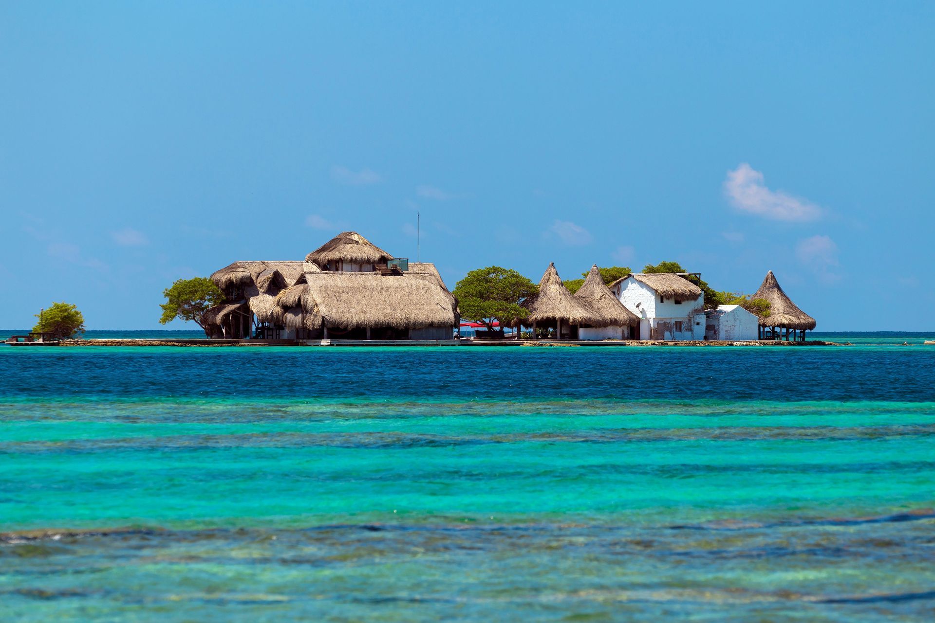 Pequeña isla con edificios con techos de paja en aguas turquesas bajo un cielo azul.