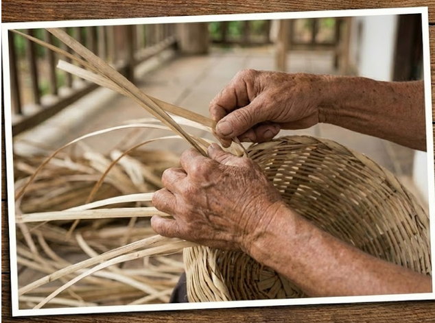 Manos tejiendo una cesta con tiras finas de tela de color claro.