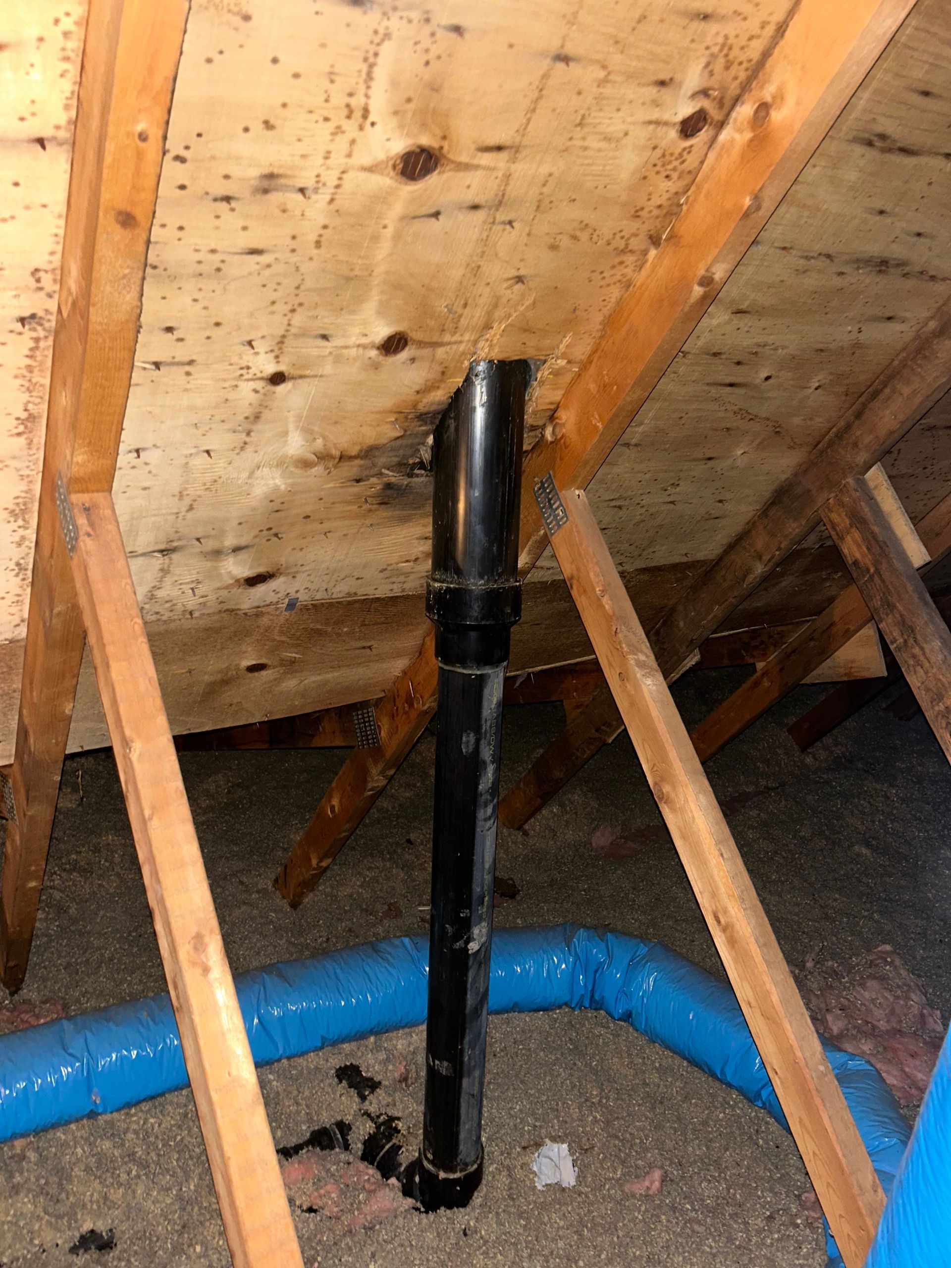 Un tuyau noir se trouve sous un plafond en bois dans un grenier.