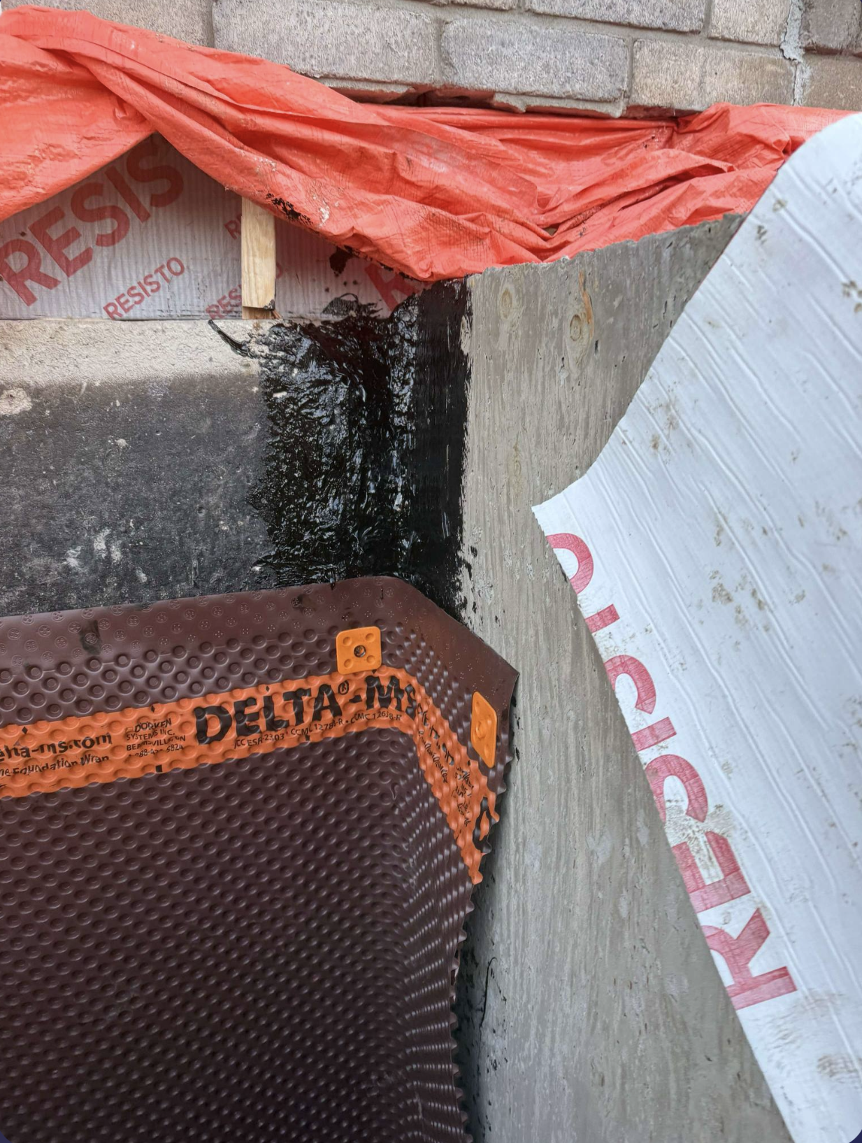 Un mur de briques est en cours d'imperméabilisation avec une membrane delta.