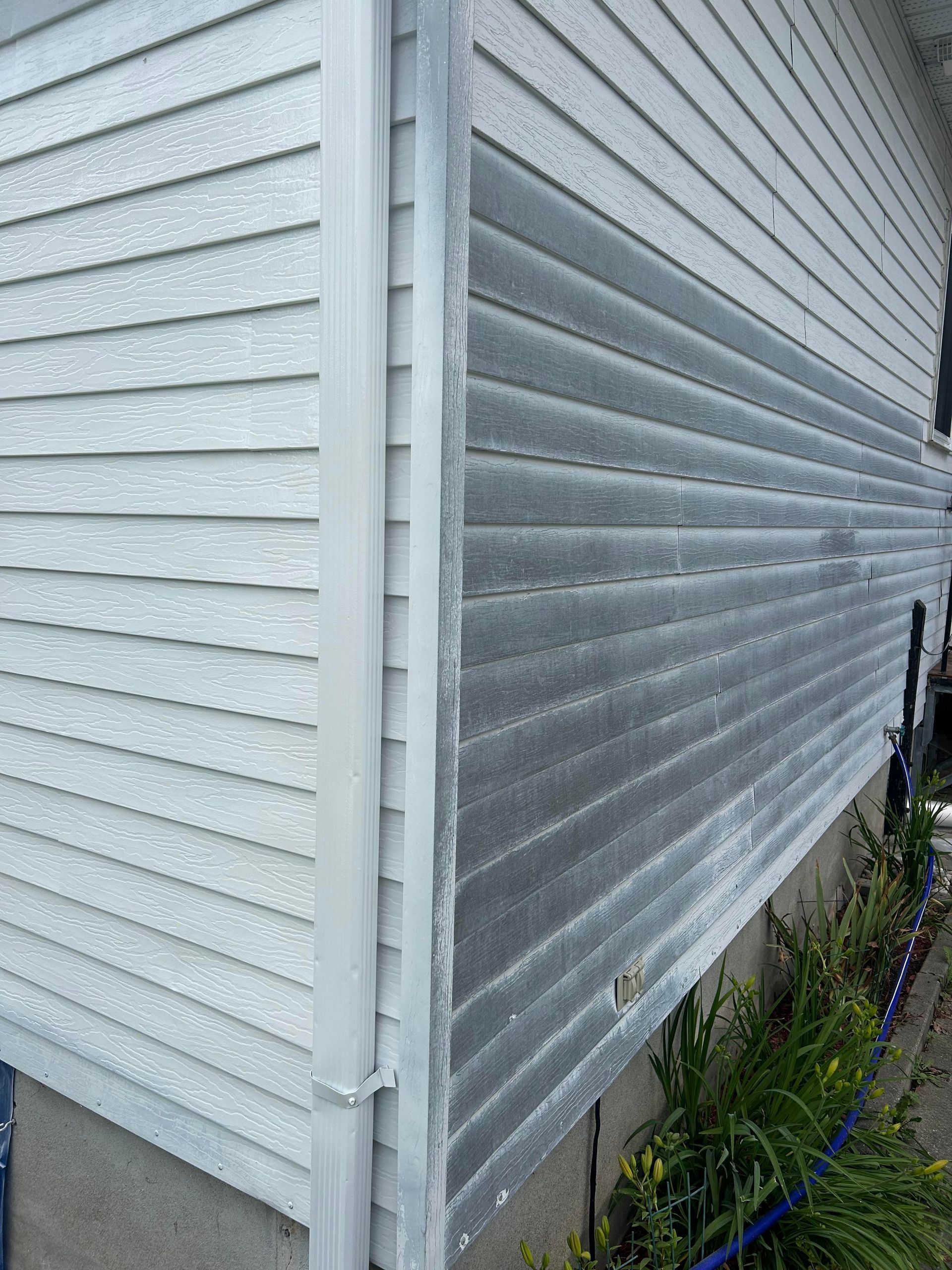 Une maison blanche avec un revêtement gris est assise à côté d'un tuyau.
