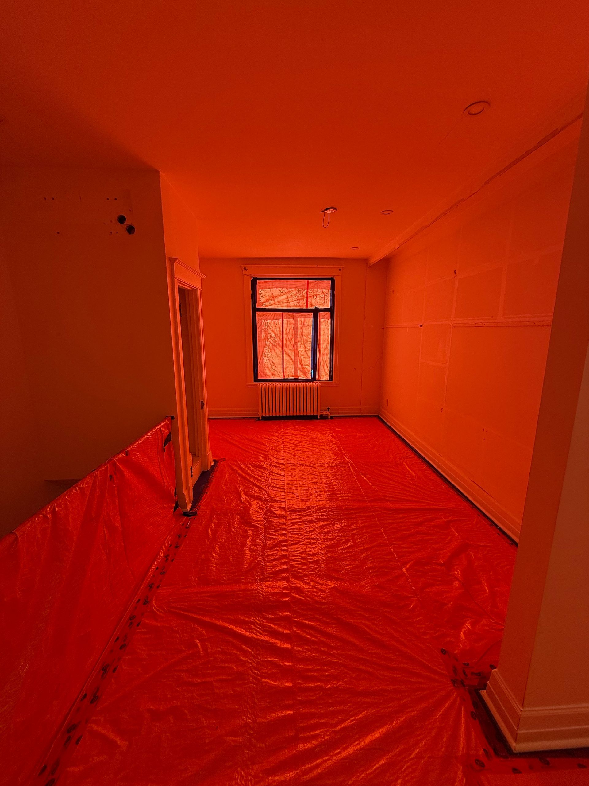 Une pièce vide avec une bâche rouge sur le sol et une fenêtre.