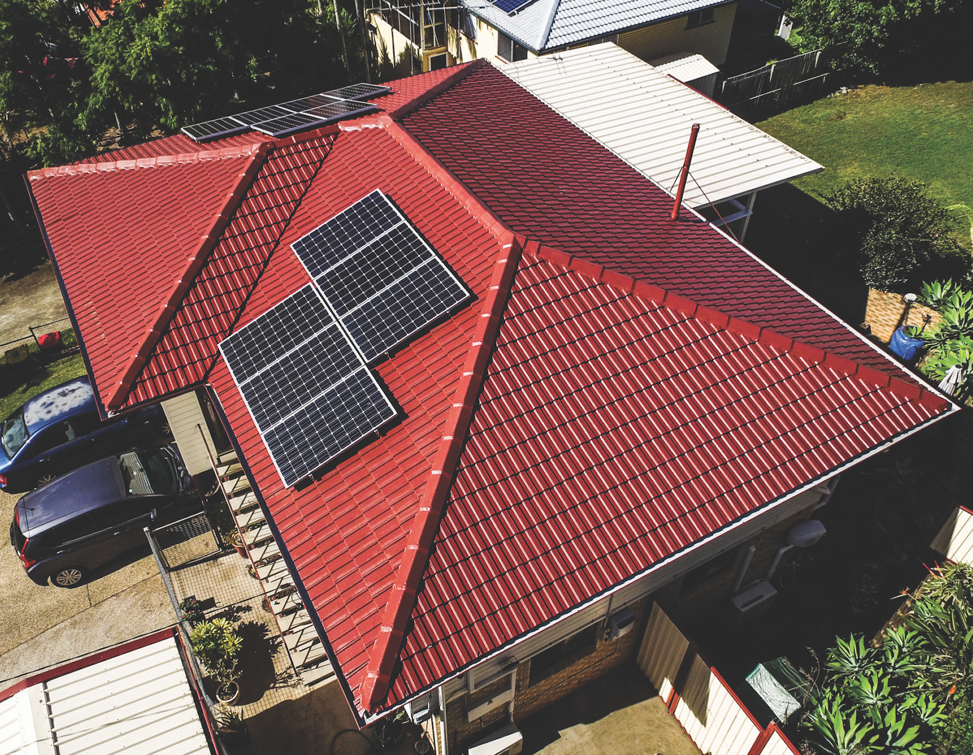Aerial view of a house with a red roof and rooftop solar panels.