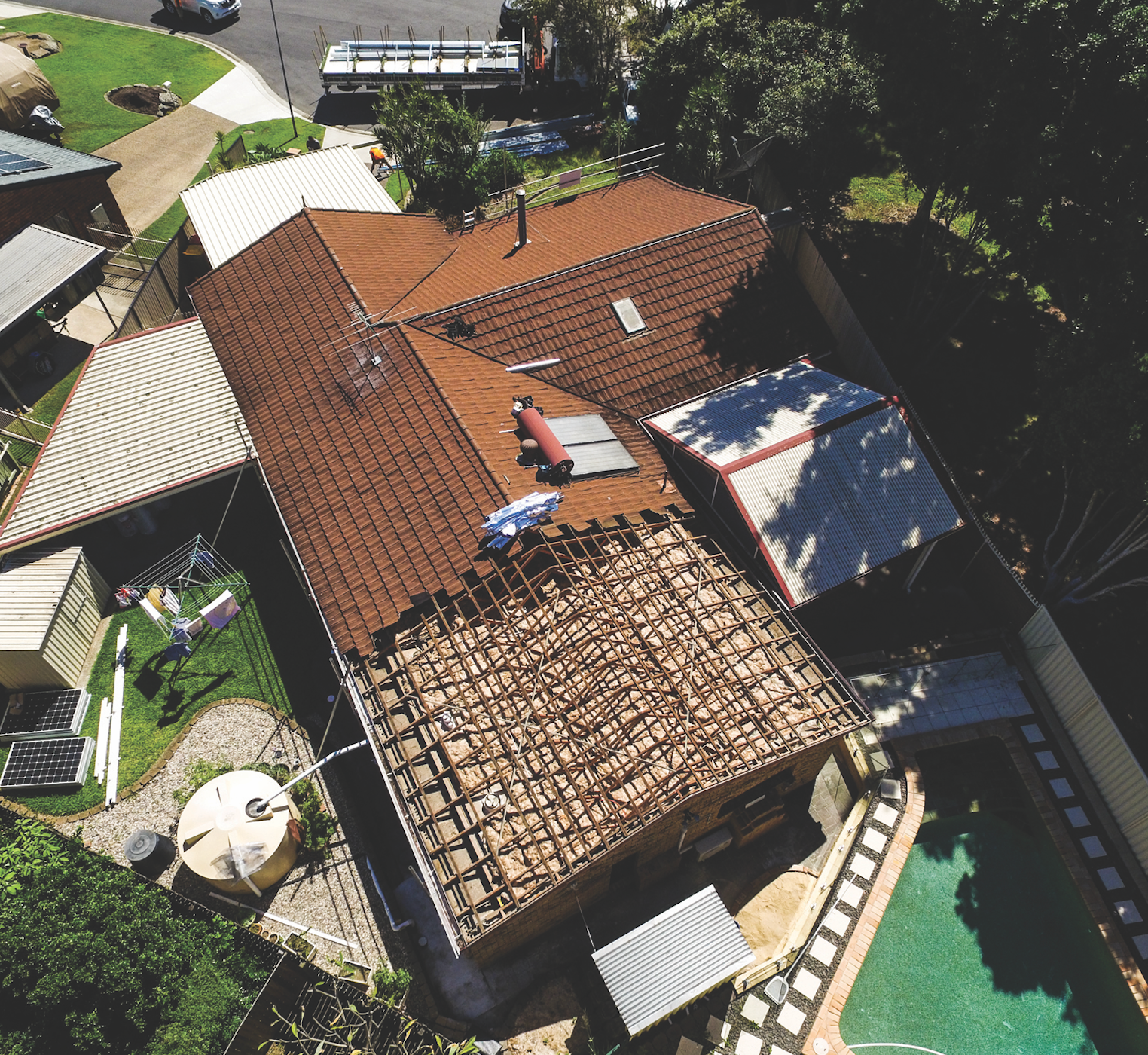 Aerial view of a house with red tile roof, solar panels, and a backyard pool, surrounded by trees.