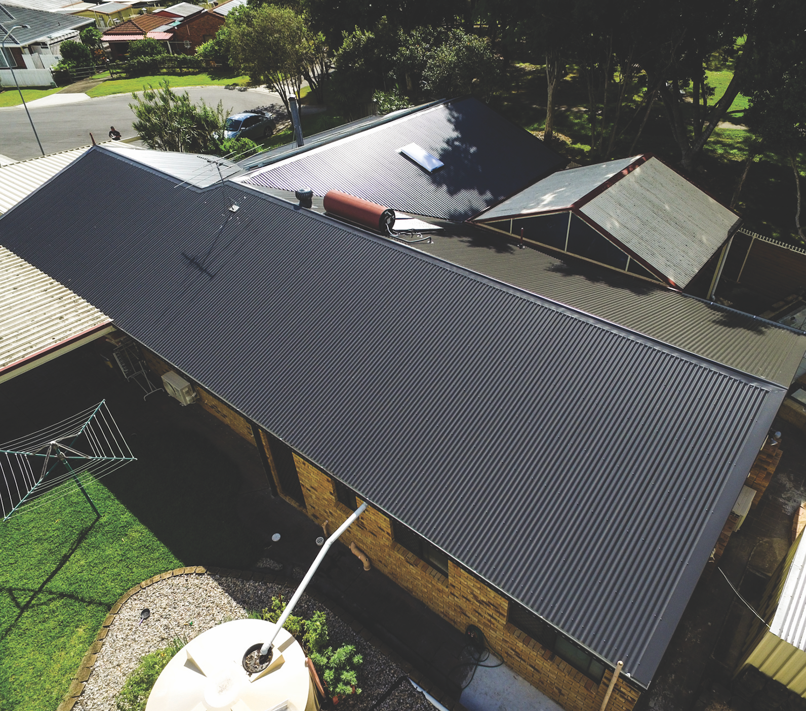 Aerial view of a house with a dark metal roof and rooftop solar panels in a suburban neighborhood