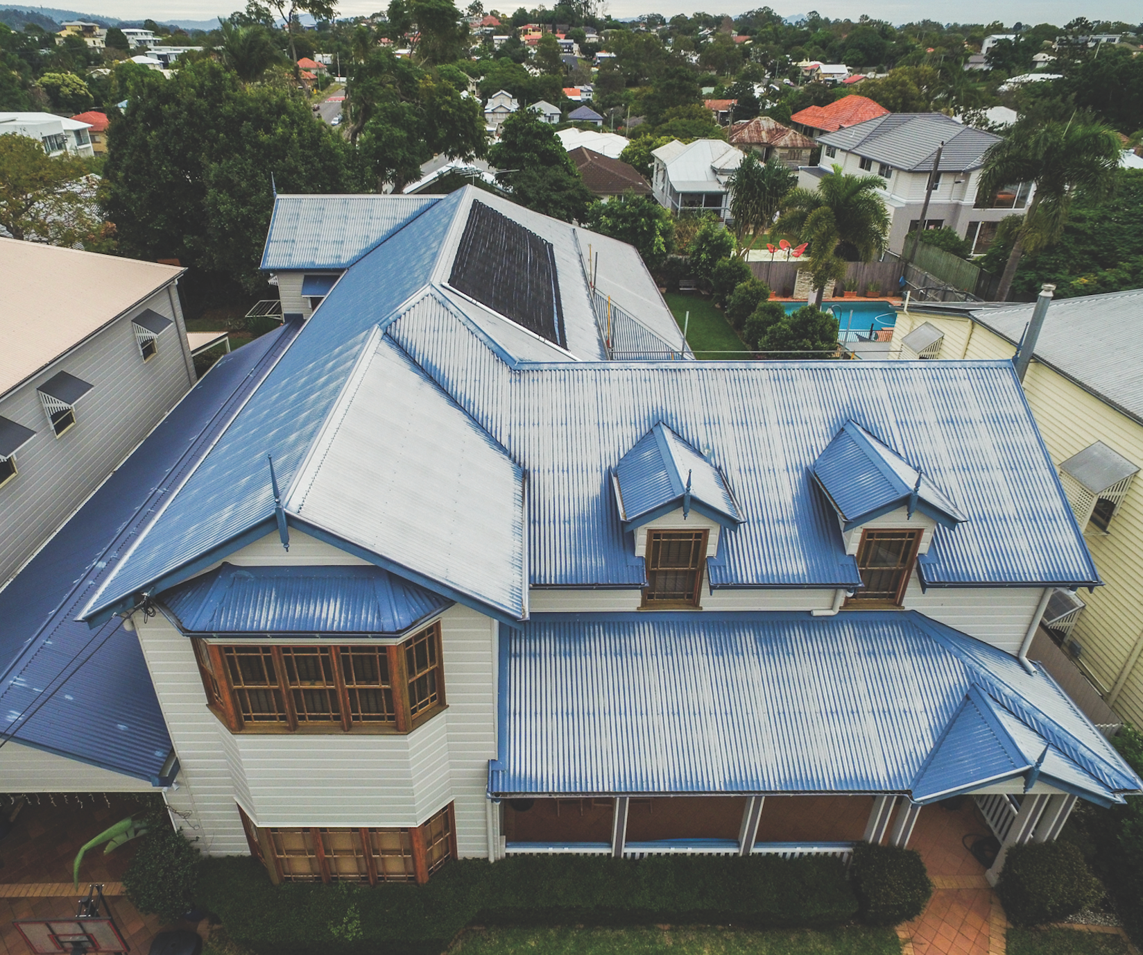 Aerial view of a brown shingled house roof with solar panels and surrounding trees