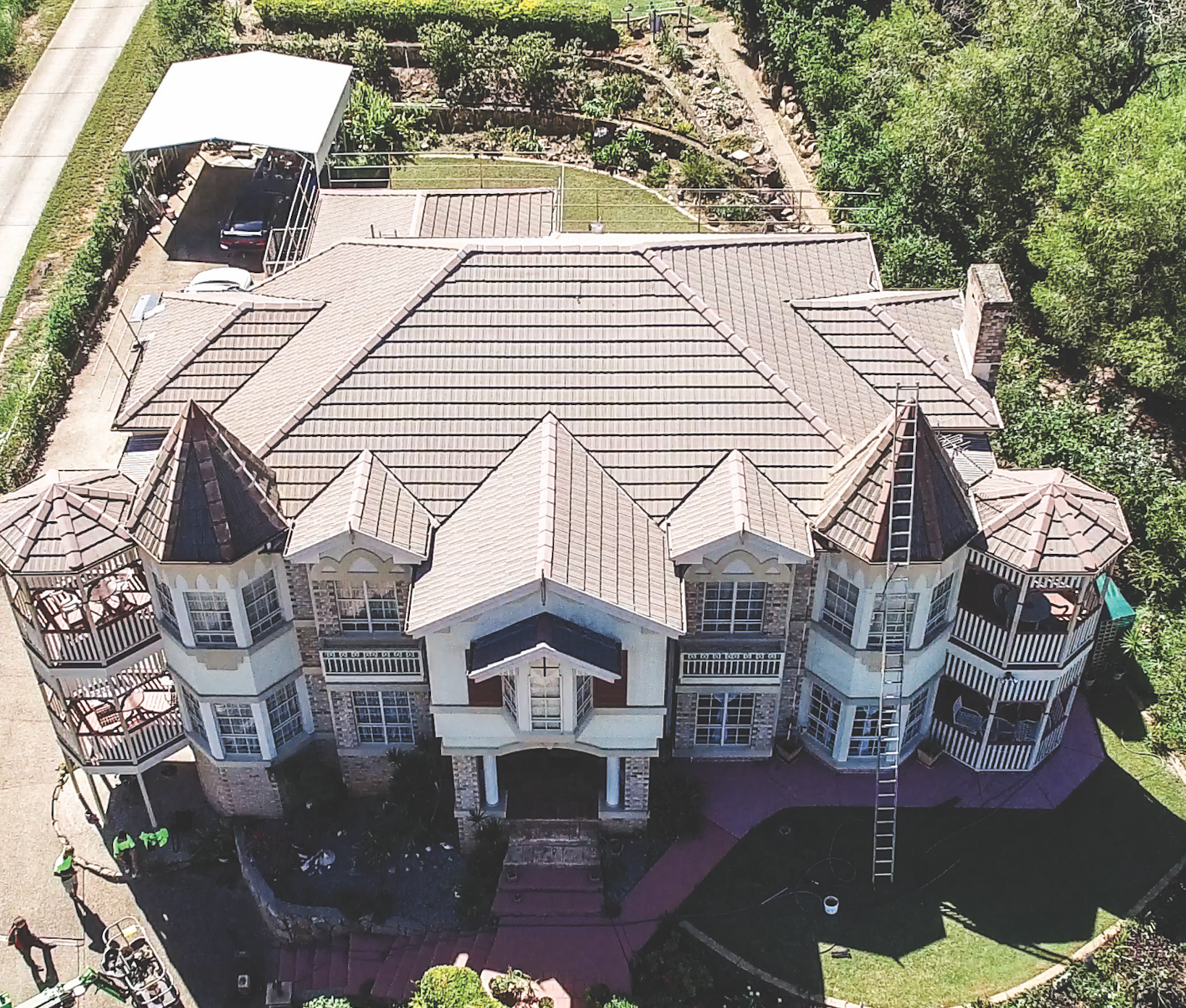 Aerial view of a brown shingled house roof with solar panels and surrounding trees