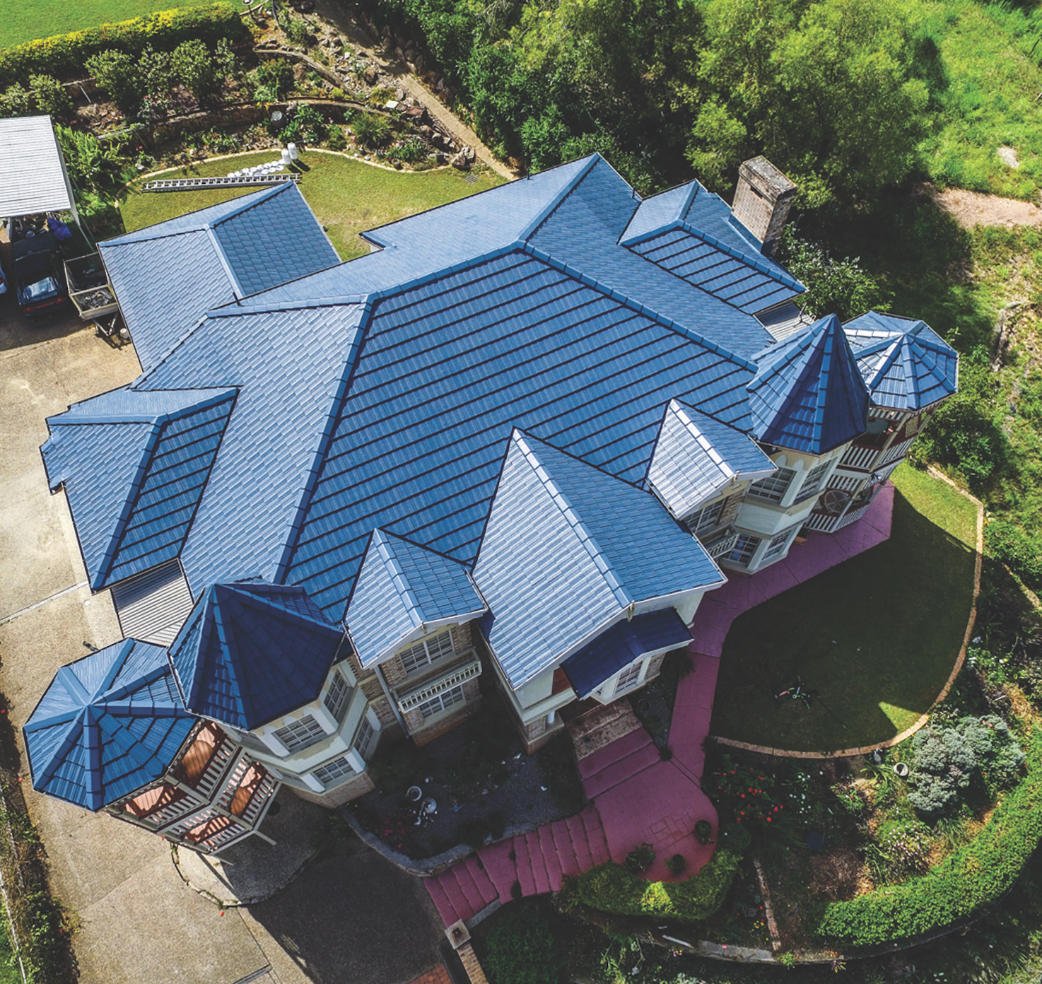 Aerial view of a large house with a blue roof, surrounded by green trees and a curved driveway.