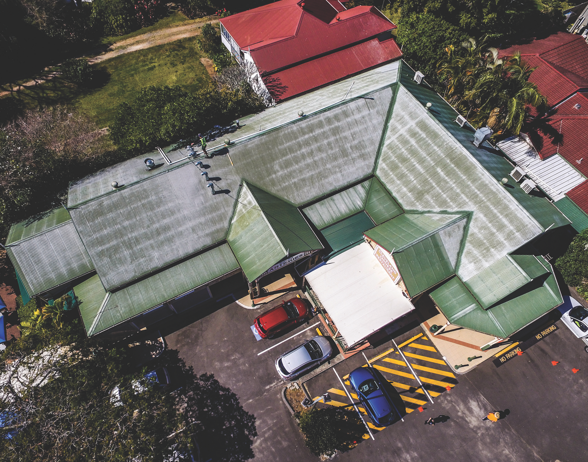 Aerial view of a parking lot beside green-roofed buildings and parked cars.