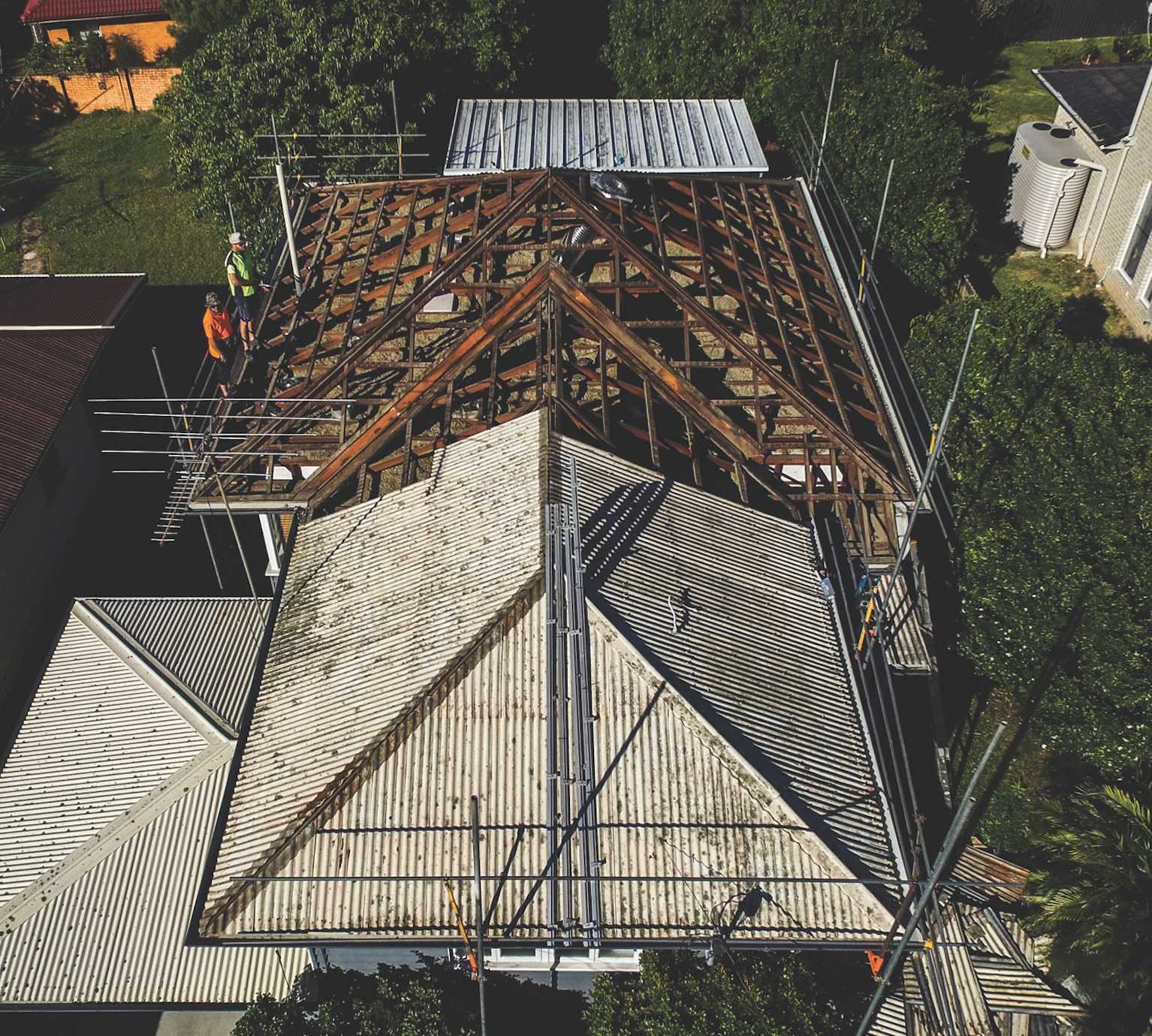 Aerial view of a brown shingled house roof with solar panels and surrounding trees