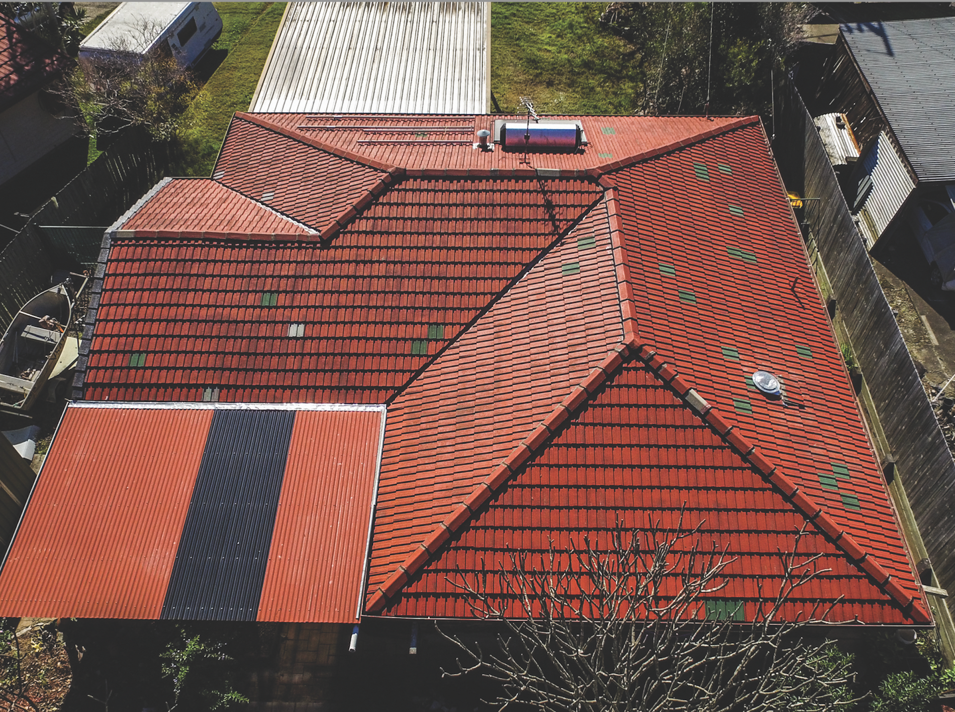 Aerial view of a red tiled house roof with a solar water heater and neighboring trees