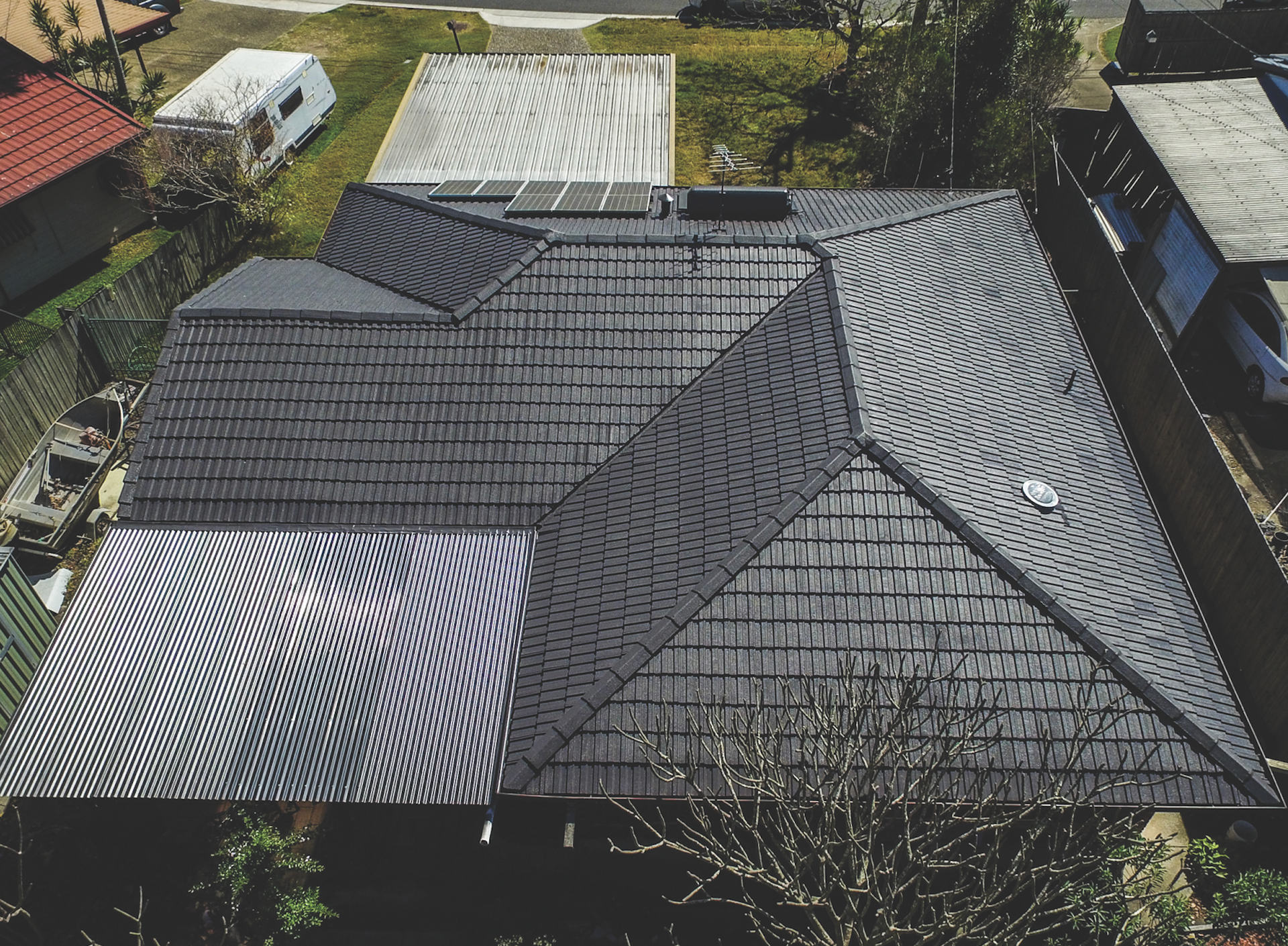 Aerial view of a house roof with dark gray and silver metal panels in a suburban neighborhood