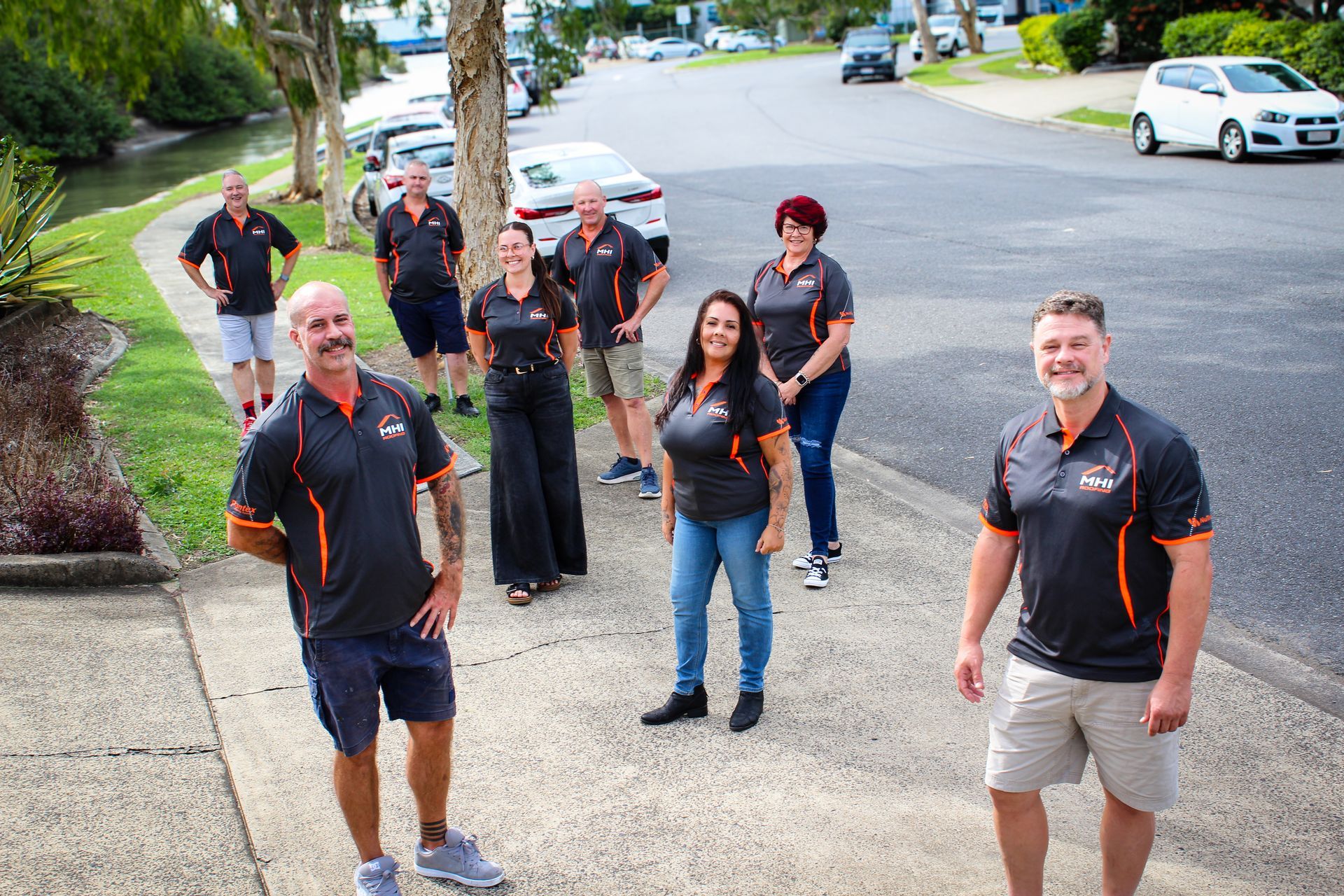 Group of people in black and orange shirts standing on a suburban street, smiling at the camera.