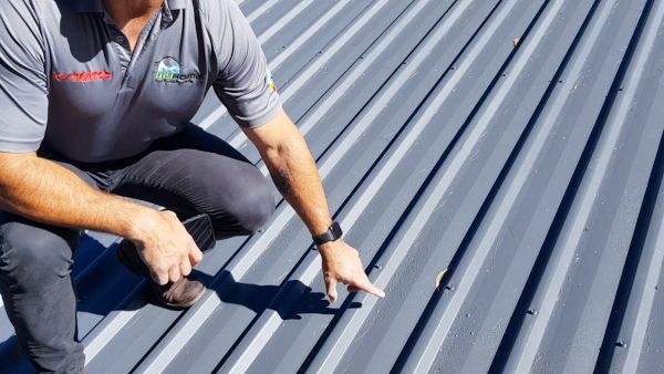 Worker inspecting gray metal roof panels with a measuring tool