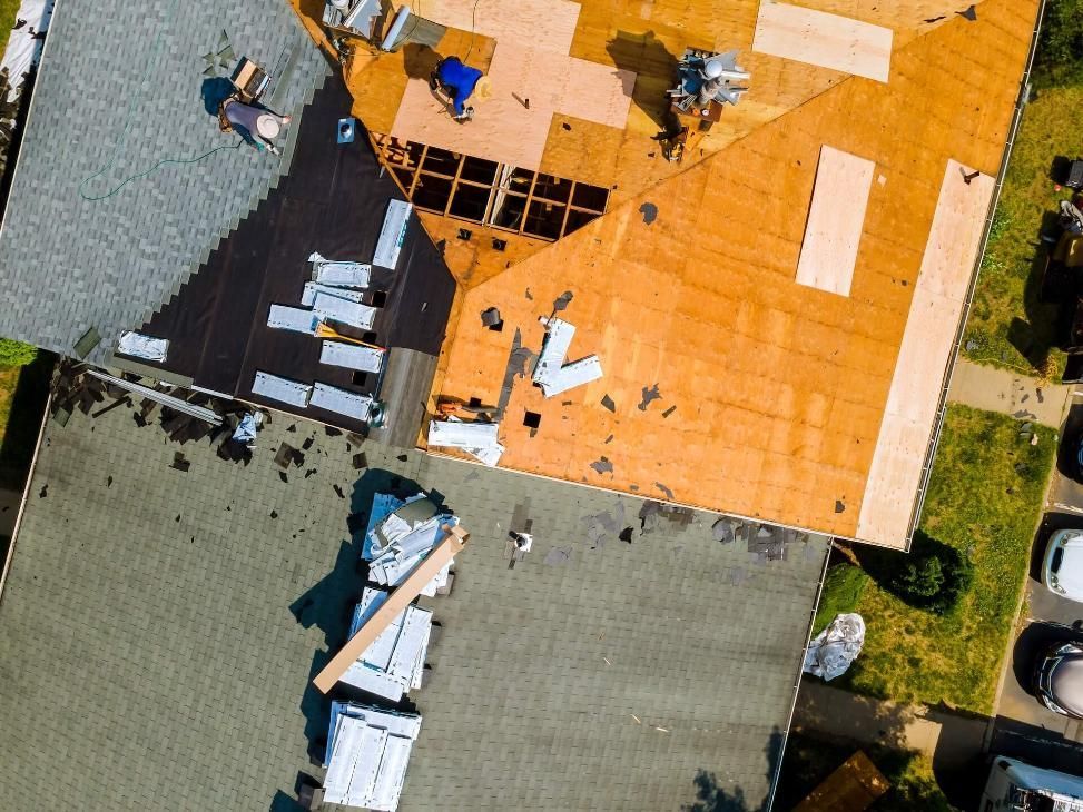Aerial view of a damaged roof with a large hole and scattered construction materials on top.