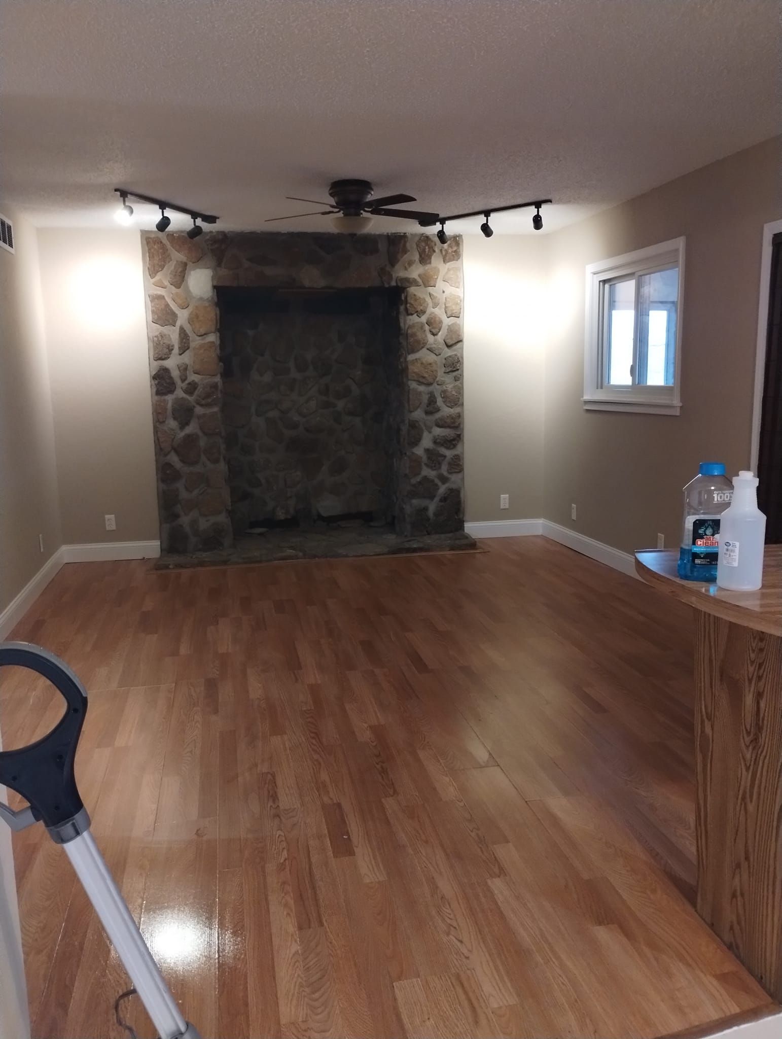 Empty living room with wood floors, stone fireplace, and track lighting.