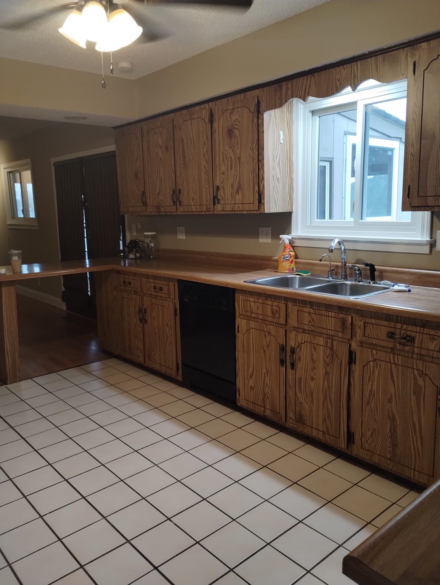 Kitchen with wood cabinets, black dishwasher, and white tile floor. Window above the sink.