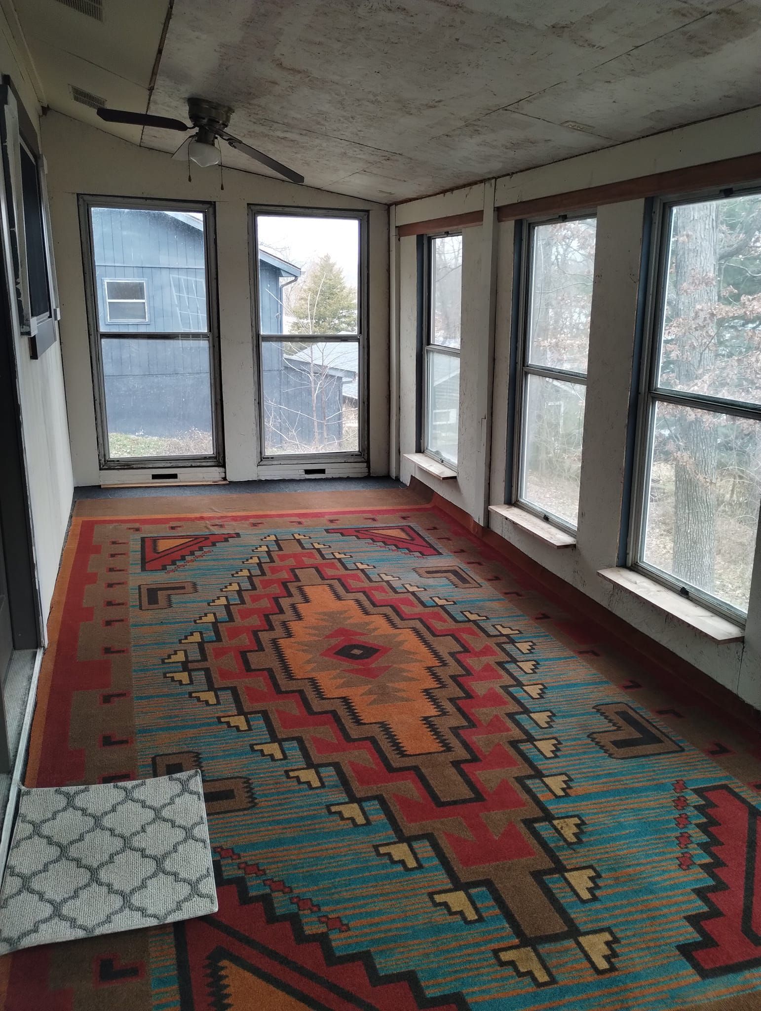 Sunroom with colorful patterned rug, windows, ceiling fan, and view of the outdoors.