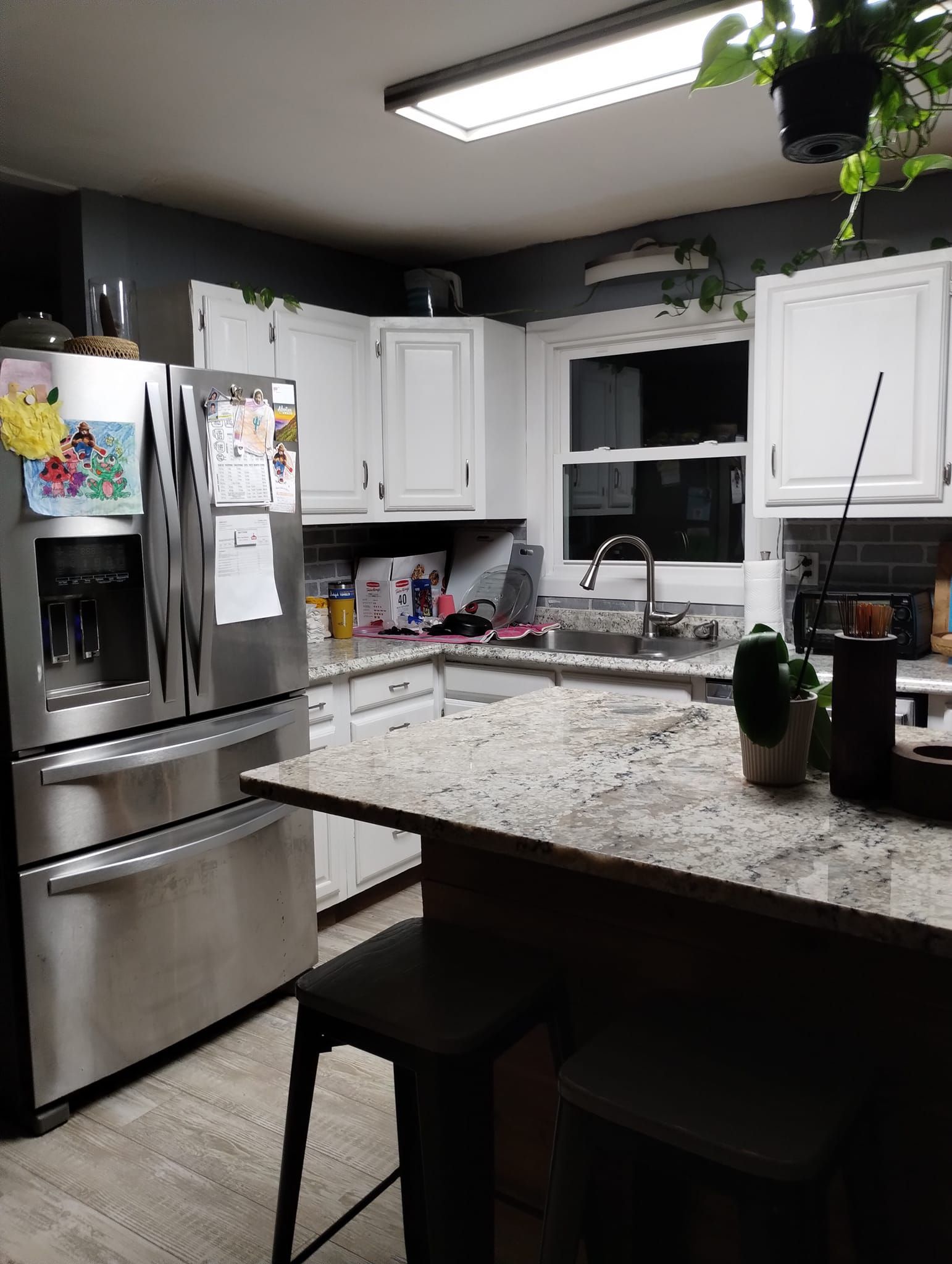 A kitchen with white cabinets, stainless steel refrigerator, and granite countertops. Two stools sit at an island.