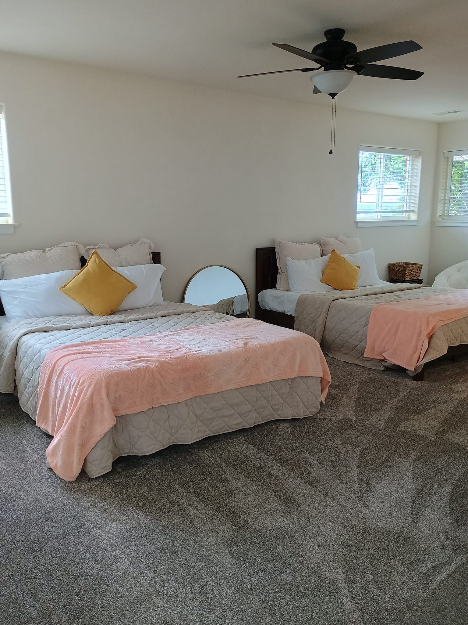 Two beds in a room, each with yellow pillows and pink blankets. Gray carpet.