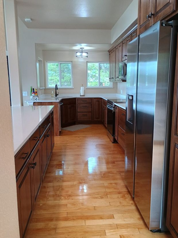 Kitchen with wood cabinets and flooring, stainless steel appliances, and two windows.