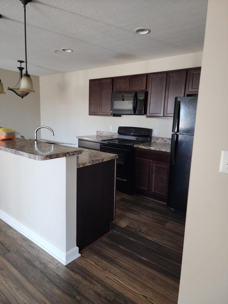 Kitchen with dark brown cabinets, black appliances, granite countertops, and wood flooring.