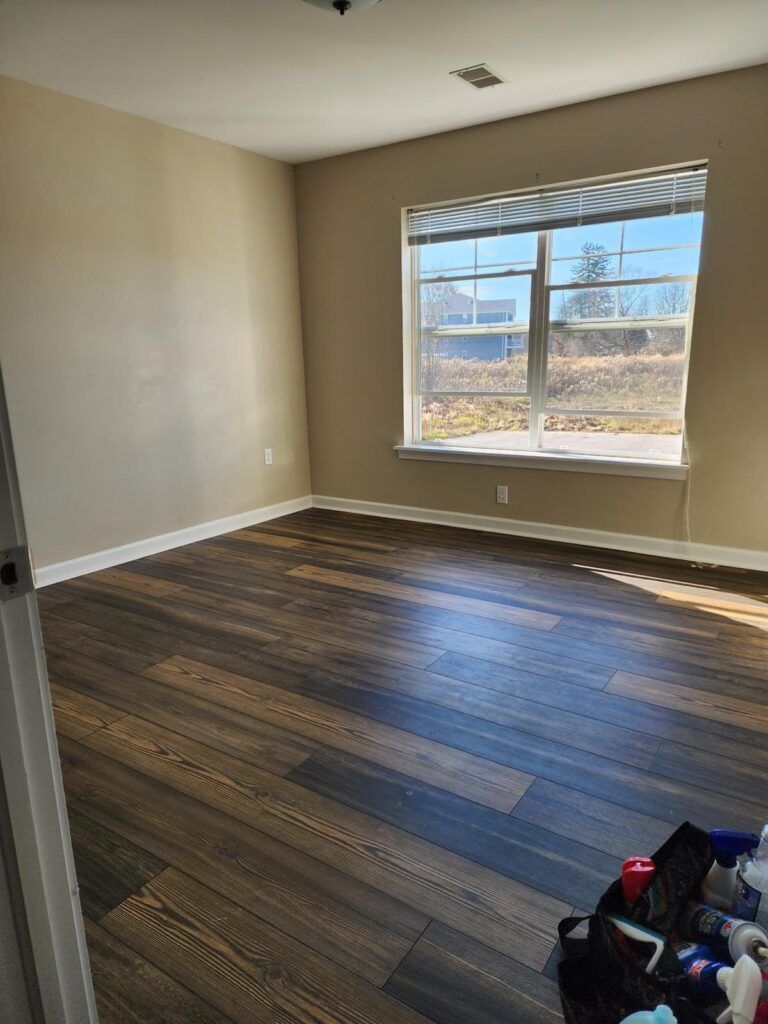 Empty room with brown wooden floor, tan walls, and a window with a view.