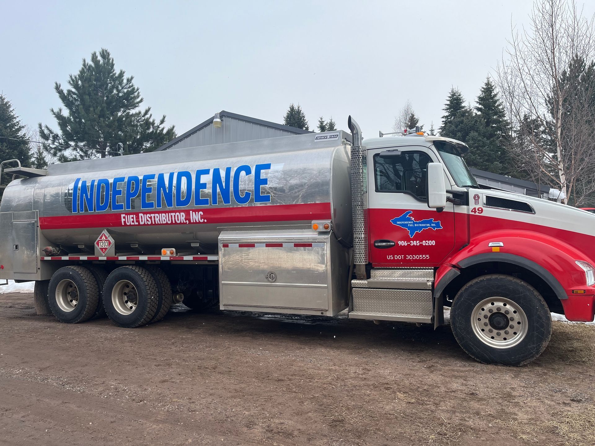 Person in blue overalls and gloves connecting a red hose to a tanker truck for refueling.