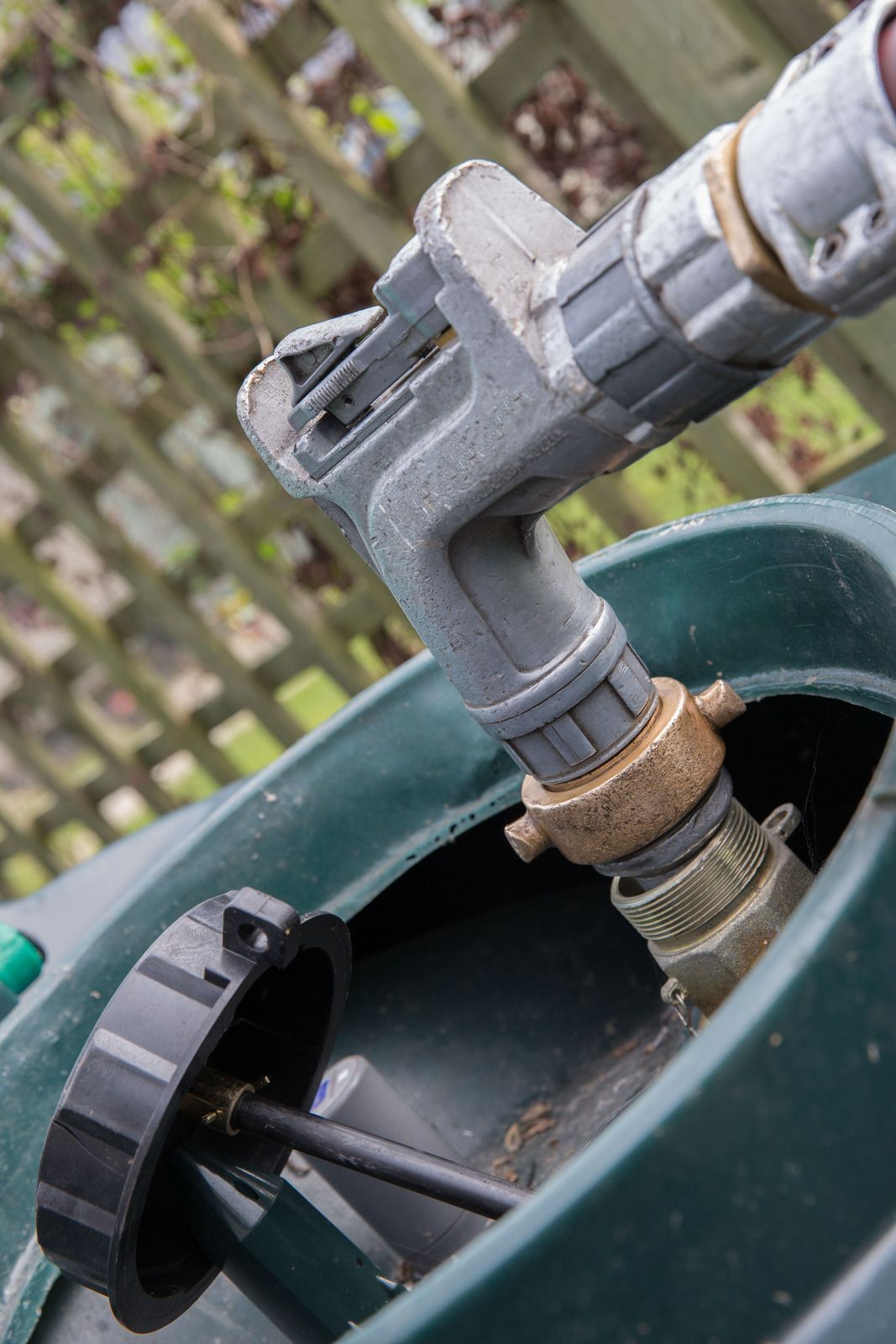 Fuel nozzle inserted into a green oil tank for refilling, cap open.