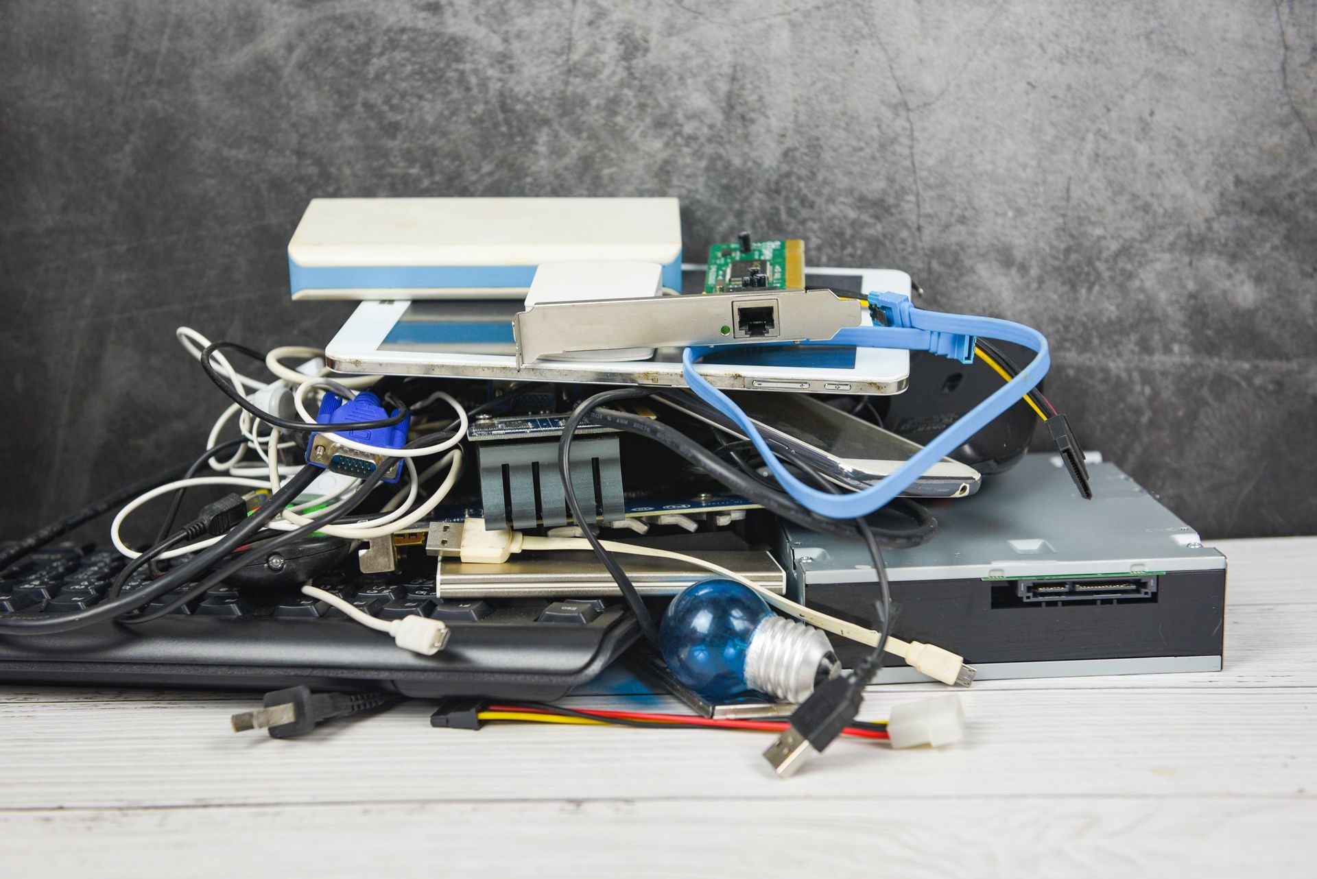 Pile of electronic waste with cables, hard drives, circuit boards, and a light bulb.
