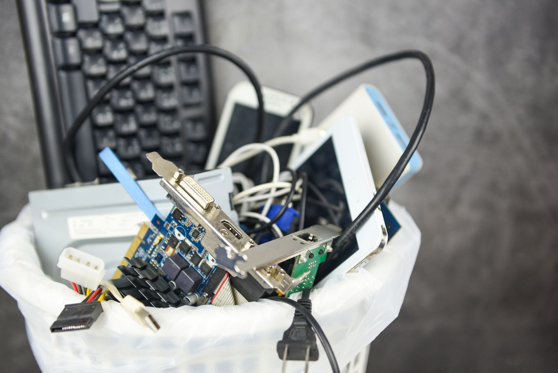 Trash bin filled with old electronics, cables, and computer parts.
