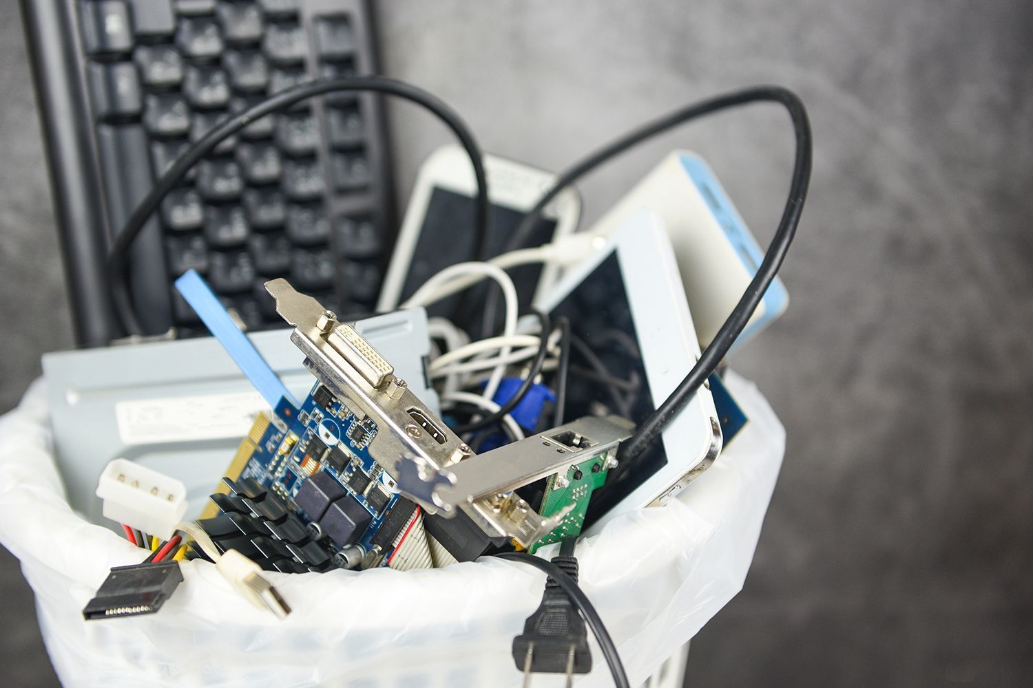 Discarded electronics and cables overflowing from a bin for e-waste disposal.