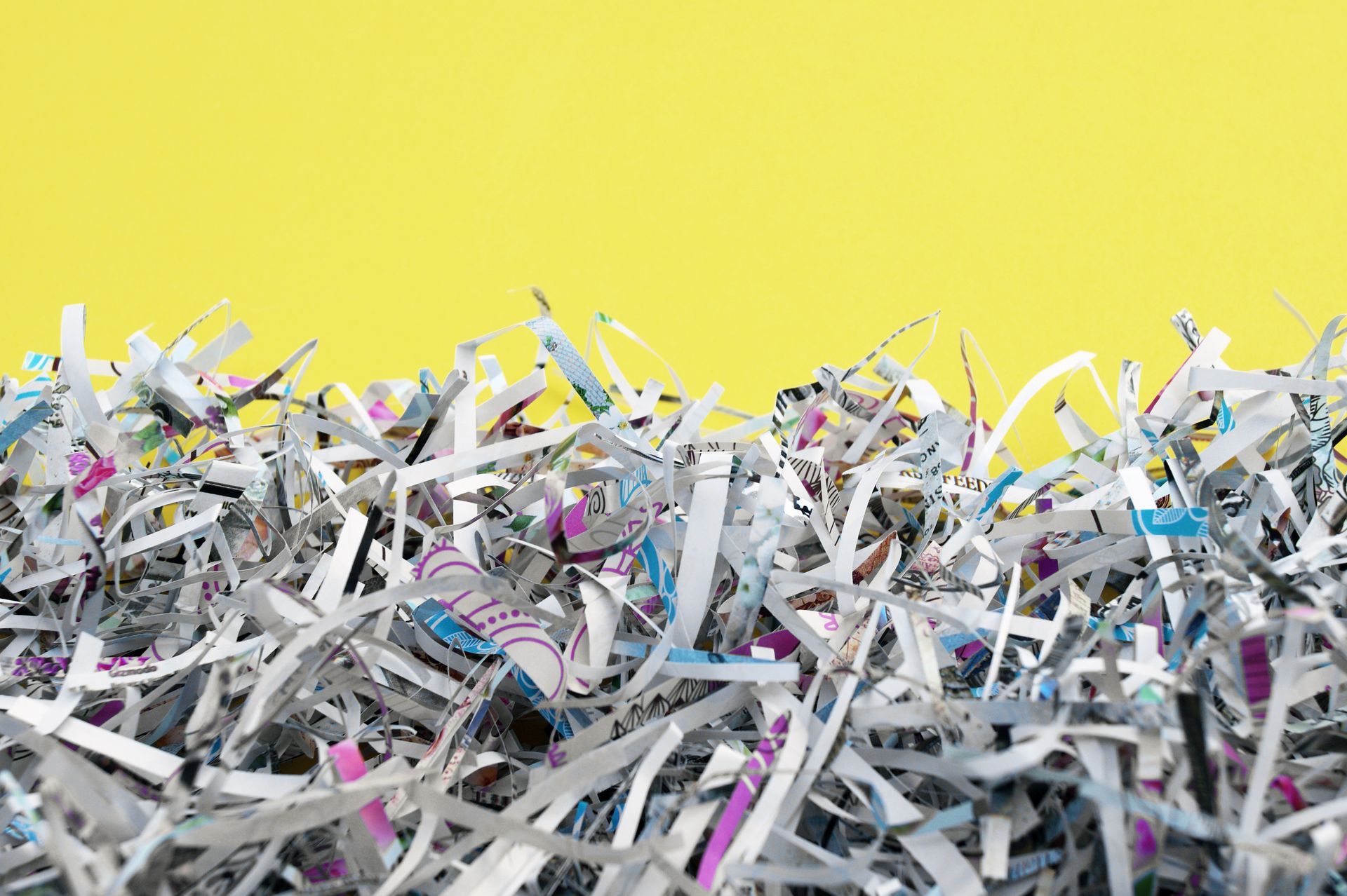 Pile of shredded paper strips in various colors and text fragments.