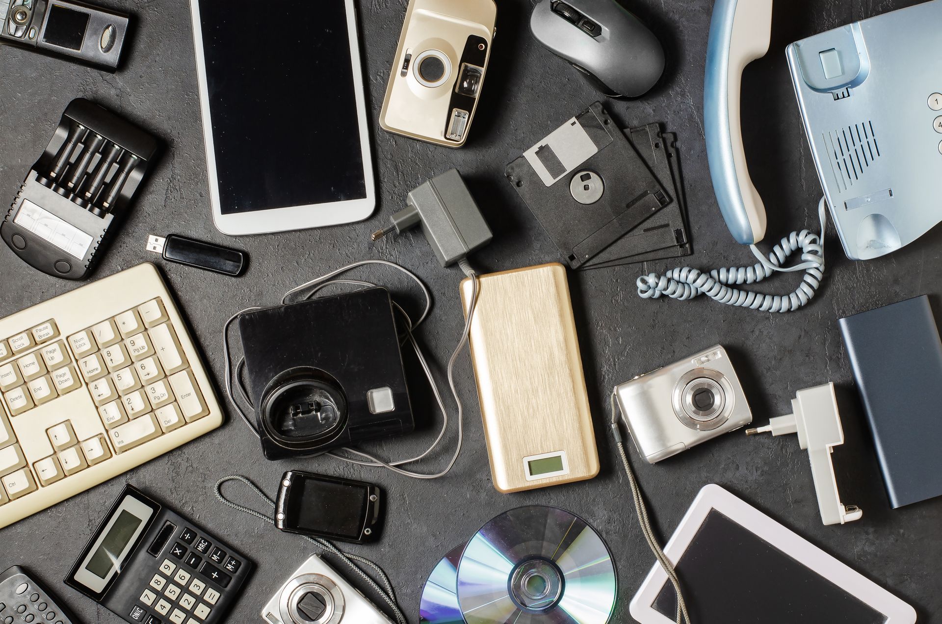 Assorted old electronics and gadgets around a recycling symbol on dark surface. Assorted old electronics and gadgets around a recycling symbol on dark surface.