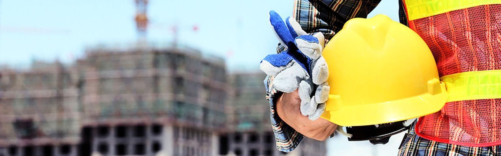 Un trabajador de la construcción sostiene un casco y guantes en un sitio de construcción.