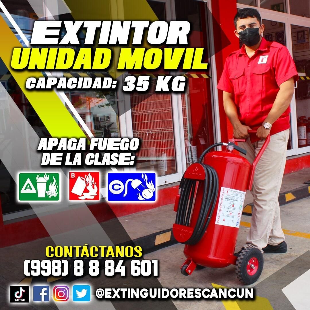 Un hombre con máscara empuja un extintor rojo sobre ruedas