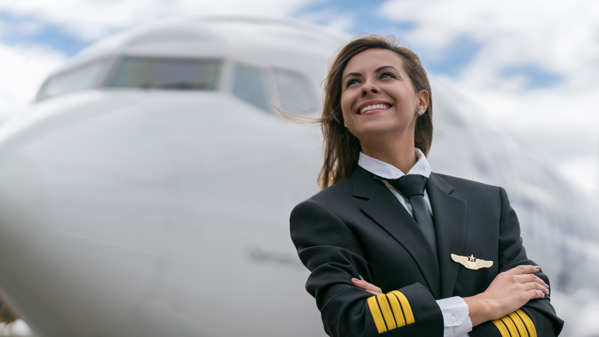 Woman pilot in uniform smiles in front of a passenger airplane.