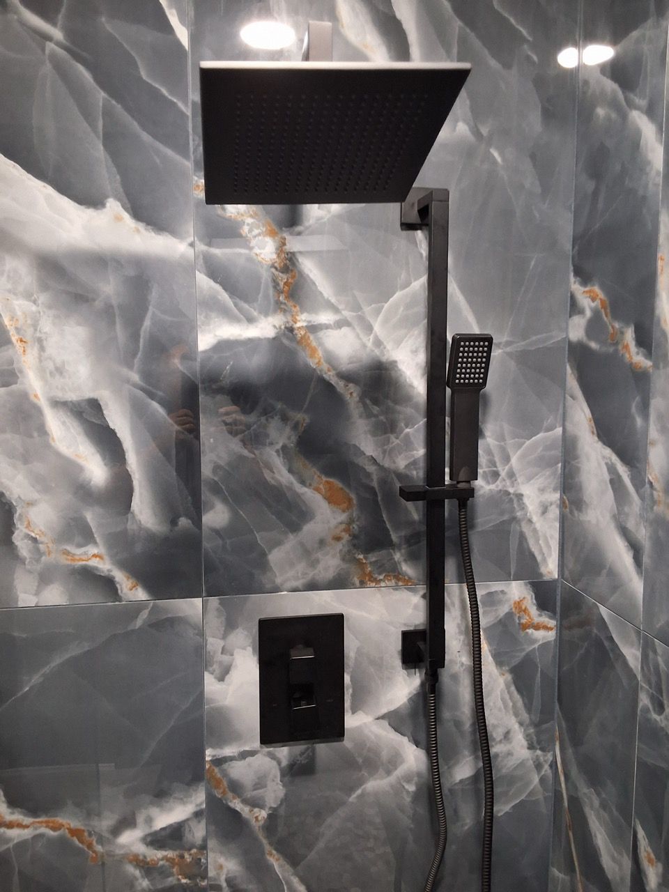 Black rainfall showerhead and handheld shower on gray marble tile wall.